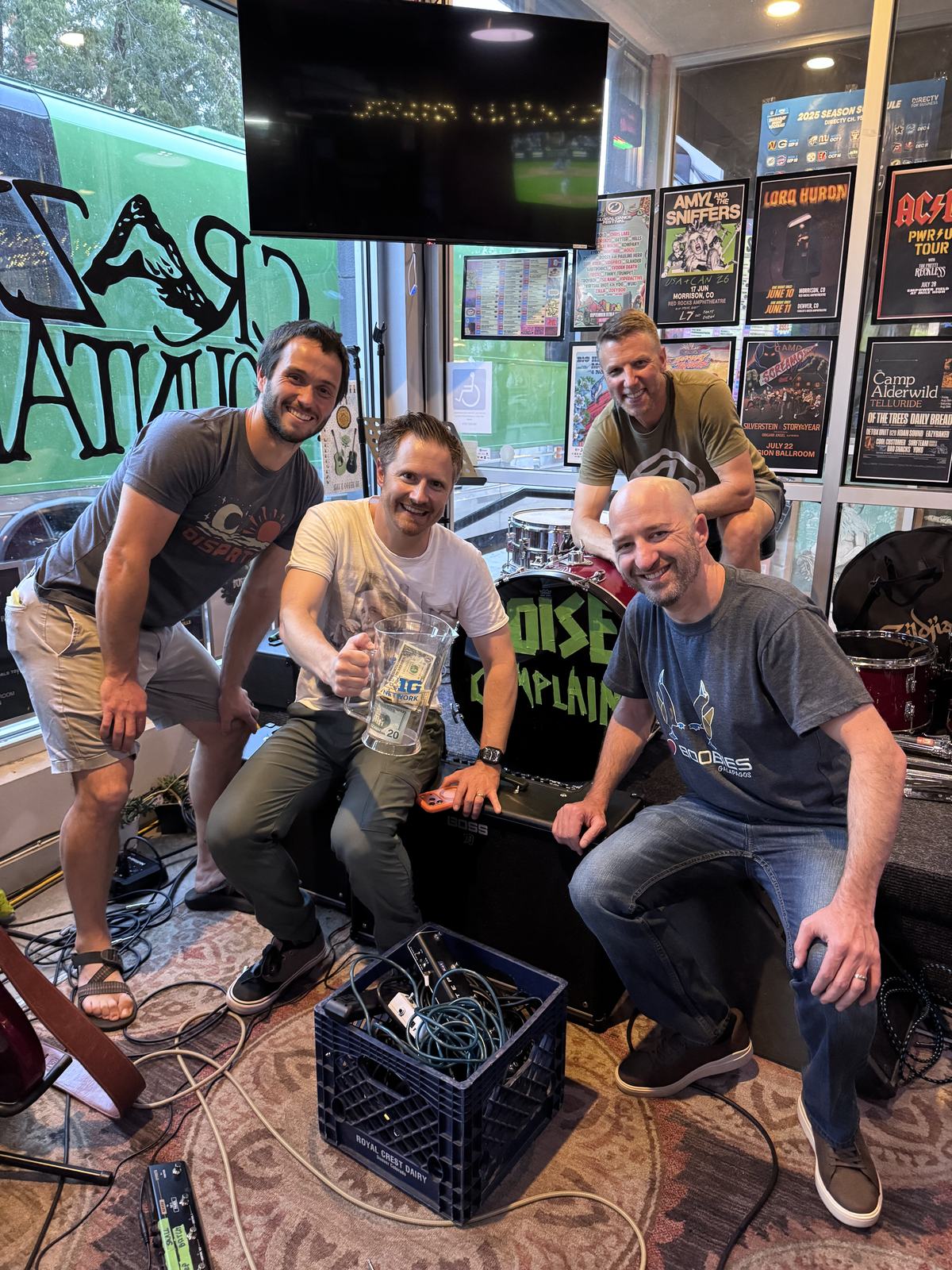 The four members of Noise Complaint crouched around their gear after a set, holding a pitcher of tip money.